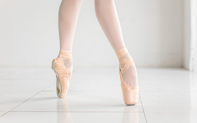 Ballerina feet in ballet pointe shoes dancing in white room