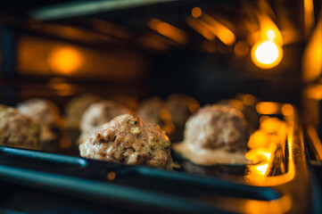View into the oven on the baking tray for meatballs. Little light, light only from the oven. Shallow depth of field, blurred background.