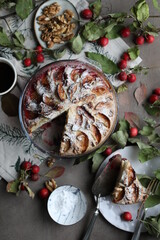 Apple charlotte sprinkled with powdered sugar in a glass baking dish. Autumn pastries on the table with a tablecloth and branches with leaves.