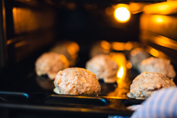 View into the oven on the baking tray for meatballs. Little light, light only from the oven. Shallow depth of field, blurred background.