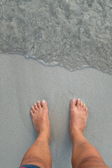 Feet on the grey sand of a beach shore