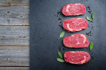 Raw dry aged wagyu rib-eye beef steaks with herb and black salt offered as top view on a black board with copy space left