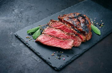 Barbecue dry aged wagyu rib-eye beef steaks with herb and black salt offered as close-up on a black board