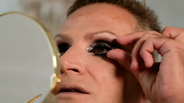 Close up of Guy applying the false eyelashes  looking at the mirror. LGBT conception 