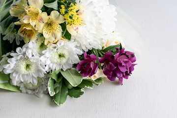 Flowers of chrysanthemums, alstroemeria, roses on a white wooden background. Place for your text.