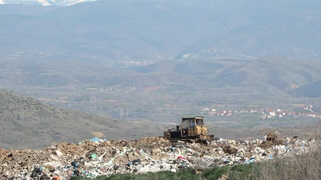 A bulldozer tractor pushes garbage from a mountain in a city dump