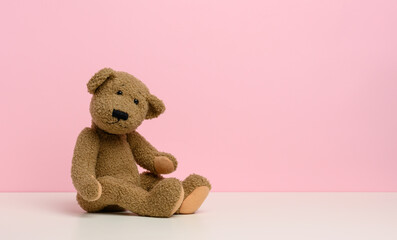 brown teddy bear with patches sits on a white table, pink background