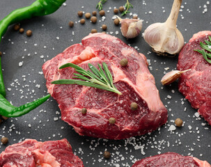 raw piece of beef ribeye with rosemary, thyme on a black table, top view