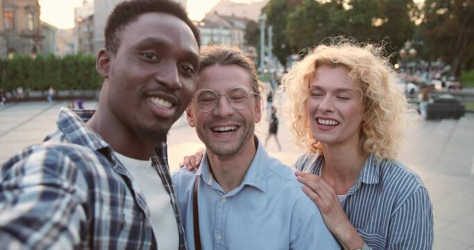 Selfie camera view of the three diverse friends talking via video call with somebody while spending time at the street and telling something emotionally