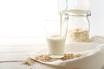 Vegan oat milk is poured into a drinking glass, healthy non dairy alternative on a light wooden table, copy space, selected focus