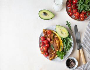 Omelette served with avocado, cherry tomatoes and arugula on ceramic plate. Healthy and tasty keto breakfast or brunch. Ketogenic diet. Top view.