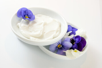 Obraz na płótnie Canvas Ointment from viola or violet flowers in white bowls, natural cosmetics concept, white gray background, copy space