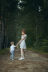 Naklejka na ściany i meble young woman mom walks with little baby son in the woods hand teaches to walk