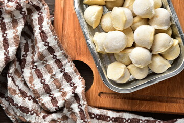Frozen homemade raw food of ravioli on wooden board table top view on cooking process semi finished pelmeni dumplings.