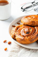 Breakfast scene with eyeglasses and newspaper. Raisin danish pastry on white plate and cup of tea. Food background.