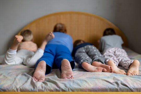 Grandmother and grandchildren lay down to rest together on huge bed. Bare feet in foreground