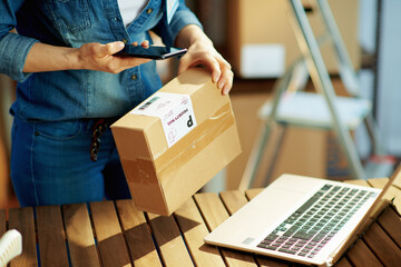 Modern female in jeans using smartphone app in warehouse