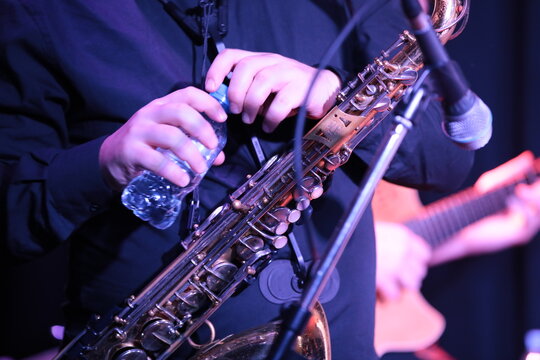 Musician playing the saxophone with a bottle of water in his hands during a break in the performance