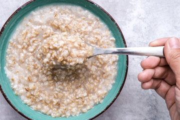 Hand holding a spoon of cooked oats porridge, healthy breakfast and dieting product close up, tasty vegan food