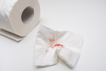 Used sheet of bloody toilet paper and a roll on white background, hemorrhoids and rectal bleeding concept