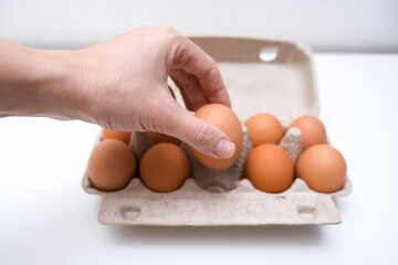 Hand taking one brown chicken egg from a carton box, container for breakfast