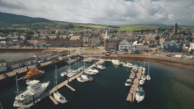 Harbor town cityscape at marina aerial. Downtown streets with traffic road. Campbeltown modern buildings at urban scenery. Green hills landscape of Scotland nobody nature at summer day