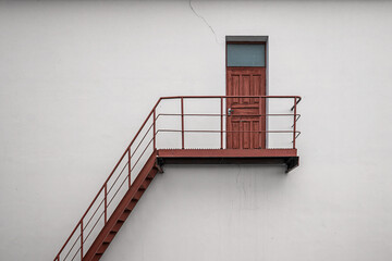 Brown vintage wooden backdoor with metal stair and handrails on white concrete building wall - obrazy, fototapety, plakaty