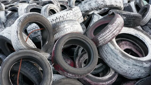 Pile of waste tires, dumped and ready for recycling. Heap of old scrap tyres, discarded and worn, painted white. Environmental protection and rubber pollution prevention. 