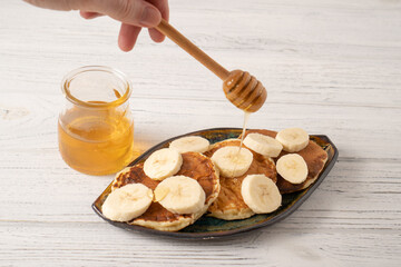 Cheese pancake with banana and honey. Ricotta pancakes with yoghurt and banana. Hand holding honey dipper