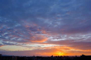 Obraz na płótnie Canvas 都市の夜明け、早朝ビルの隙間から太陽が昇り辺りはオレンジ色に染まる。ビルはシルエットに浮かぶ。