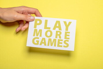 female hand holds a piece of paper with the inscription play more games in yellow writing over...
