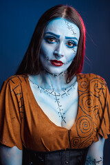Halloween makeup woman model portrait with blue tones and brown blouse with red lipstick feeling sad looking at camera