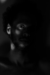 Portrait of a man. bare chest. in the dark. looking the camera. low light. black and white