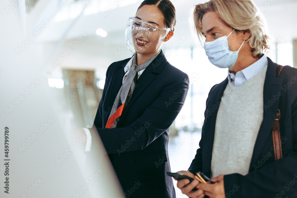 Wall mural Flight attendant assisting traveler with self check in at airport