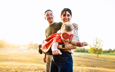 Happy family playing together outside - Kid in a superhero costume having fun with mother and dad...