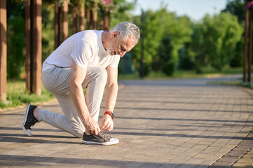 A mid aged man in sportswear lacing his snickers