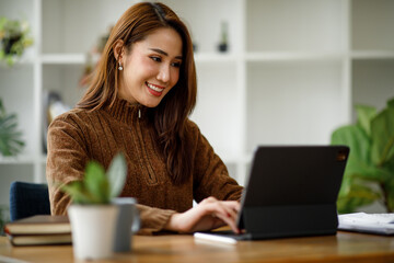 Portrait of Young Asian woman hand freelancer is working her job on computer tablet in modern office. Doing accounting analysis report real estate investment data, Financial and tax systems concept.