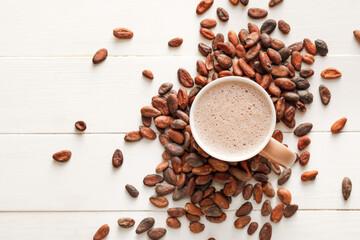 Cup of hot cocoa drink and beans on light wooden background
