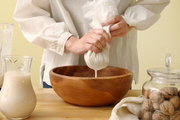 Woman preparing tasty walnut milk on kitchen table, closeup