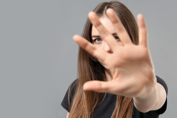 Young woman showing STOP gesture on grey background. Concept of harassment