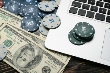 Poker chips, laptop and dollar banknotes on table, closeup
