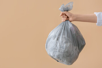 Woman holding bag with garbage on color background