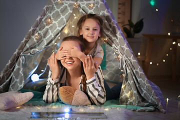 Little girl closing eyes to her mother in play tent at home