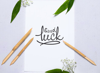 Paper with text GOOD LUCK, dip pens and flowers on white background