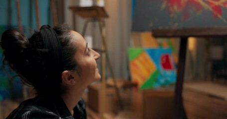 Close-up on the face of a positive woman sitting on the floor, she is looking at the picture with a smile on her lips, thinking about making it more interesting, adding another color - Powered by Adobe