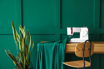 Tailor's workplace with sewing machine, cloth and houseplant near green wall