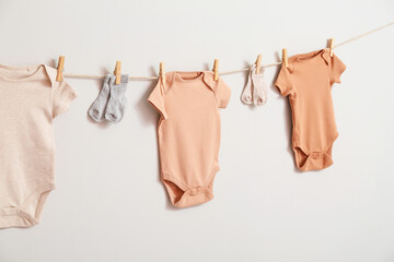 Different baby clothes and socks hanging on rope against white background