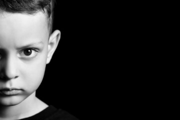 Black and white portrait of angry little boy on dark background
