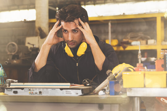 Young Indian engineer looked tired and sat stressed on his workbench with many things and tools cluttered : Young engineers have a headache with excessive factory maintenance work.