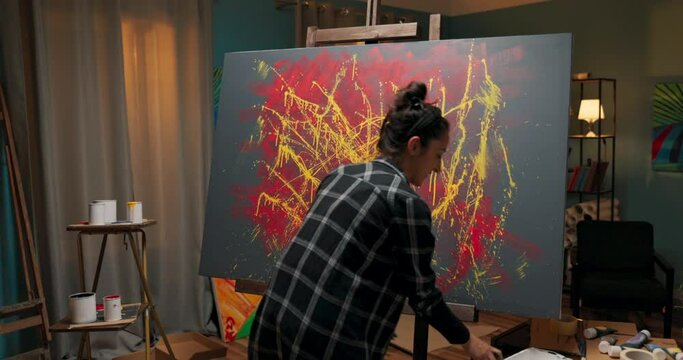 Talented painter spends an evening in front of the canvas, takes her time to work abstractly, in her hand holds a can of white paint and a brush, the girl sprays color on the painting, artistic vision